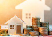 Coin stack on international banknotes with house model on table